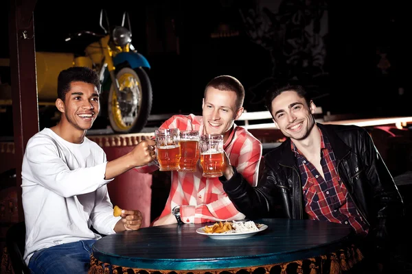 Happy friends clinking with beer mug in pub, smile . — Stok Foto