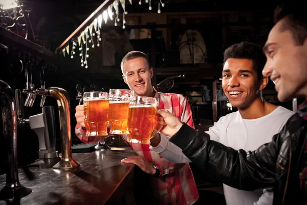 Happy friends clinking with beer mug in pub, smile . — Stok Foto