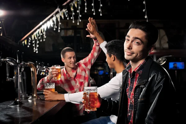 Amigos felizes clinking com canecas de cerveja no pub, sorrindo . — Fotografia de Stock