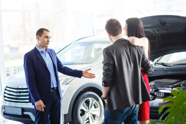 Vendedor de coches dando la llave del coche nuevo a los propietarios jóvenes — Foto de Stock