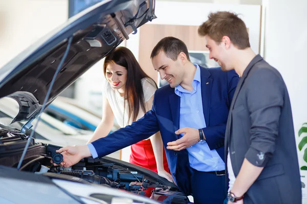 Vendedor de carro dando chave de carro novo para jovens proprietários — Fotografia de Stock