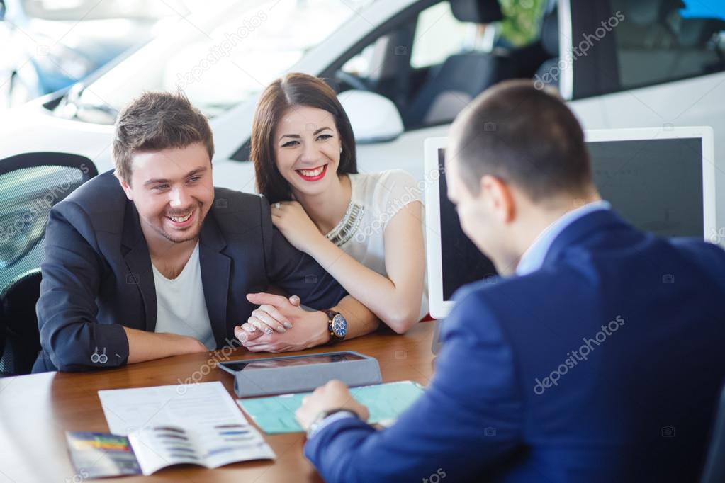 Car salesman giving key of  new car to  young  owners