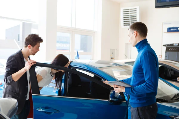 Maturo venditore mostrando nuova auto per coppia in showroom — Foto Stock