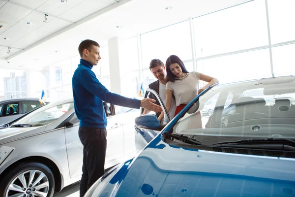 Mature salesman showing new car to  couple in showroom Royalty Free Stock Images