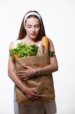 Elinde sebzeli alışveriş torbası tutan genç bir kadın.