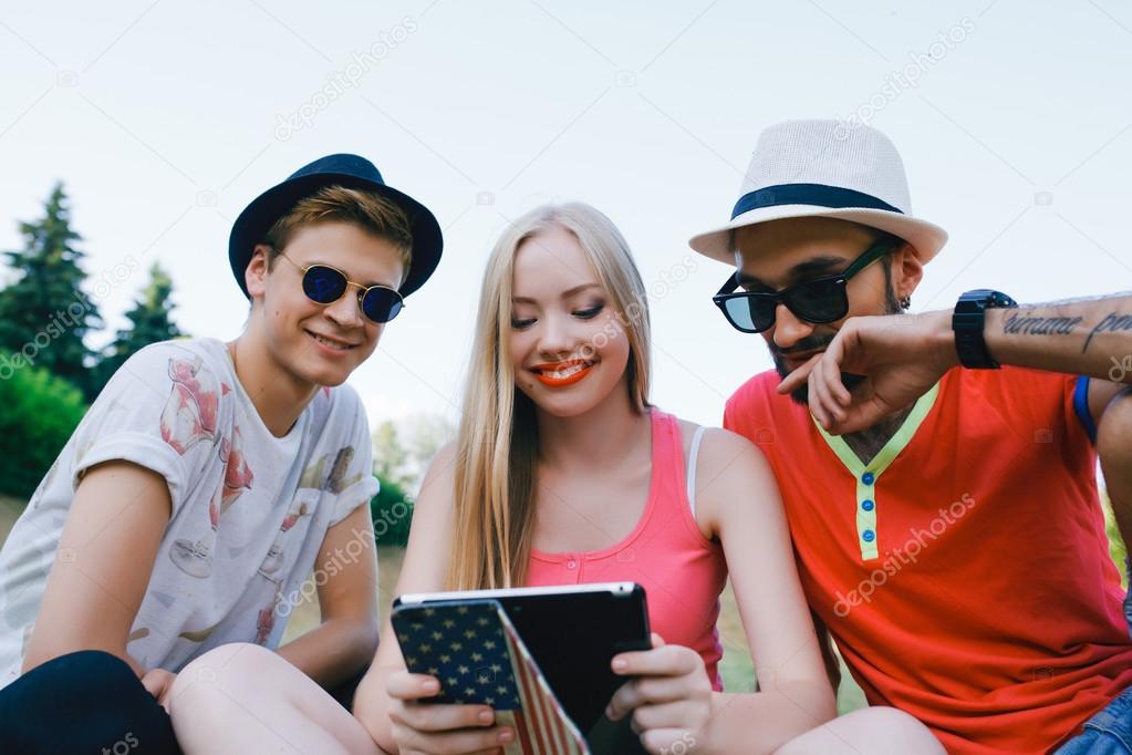 technology and people concept - group  friends with tablet pc computers , smartphone sitting  in park