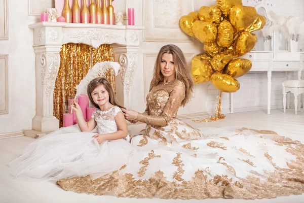 Mère et fille dans de belles robes blanches assises sur le sol. Mère peigner sa fille dans une belle chambre . — Photo