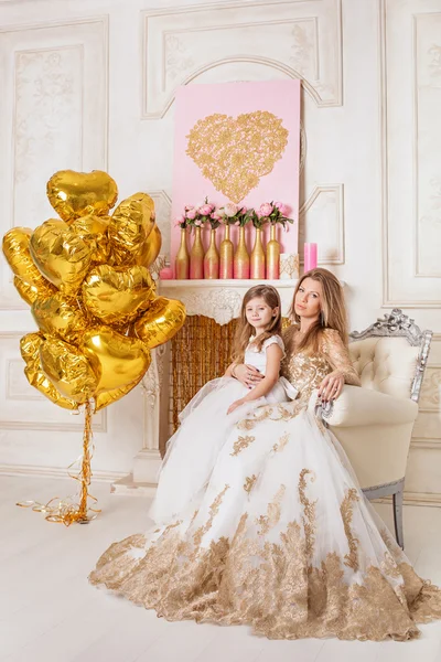 Anne ve kızı bir sandalyede oturan güzel beyaz gece elbisesi içinde.