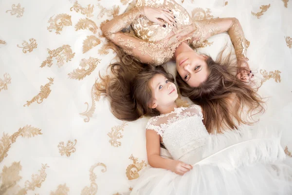 Mother and daughter lying on the floor in a beautiful white dres — Stock Photo, Image