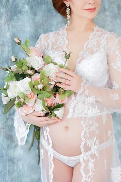 Schwangere mit Blumen im Boudoir-Kleid (Negligé) auf blauem Hintergrund. — Stockfoto