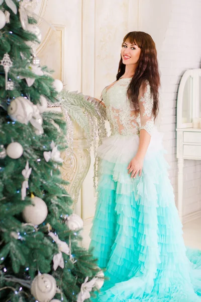 Hermosa chica sonriendo en vestido de novia de menta, de pie junto a la chimenea cerca de un árbol de Navidad . —  Fotos de Stock