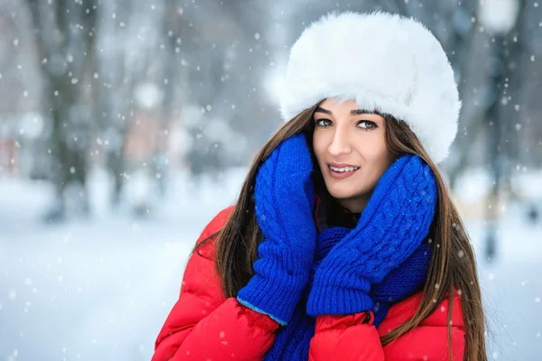 Una chica con un sombrero de piel blanca cubre su cara con las manos vestidas con manoplas azules . — Foto de Stock