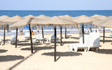 Hasır şemsiyeler denizin kenarında. Chipiona, Cadiz (İspanya).