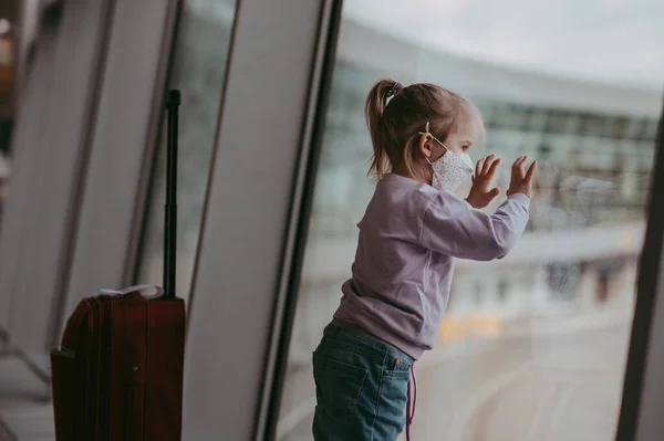 顔マスクの空港で幼児の女の子 子供はコロナウイルス発生後飛行機を見る 安全な旅行とウイルスのパンデミックで子供と一緒に飛ぶ 出発ゲートで子供 Covid 19ロックダウン後の休暇 ストック画像