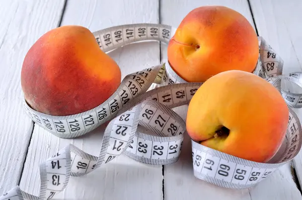 Juicy peach with measuring tape on a wooden table close-up. — Stock Photo, Image