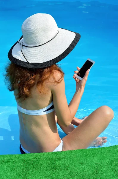 Mujer joven sexy en un sombrero con un teléfono cerca de la piscina — Foto de Stock