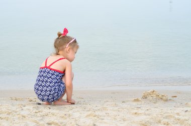 Sweet girl playing with sand on the beach, space for text/