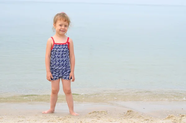 Charmig liten flicka i en baddräkt stående på en strand, utrymme fo — Stockfoto