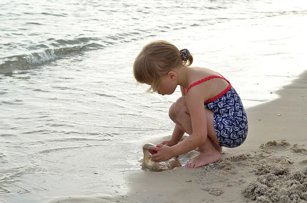 Söt flicka som leker med sand på stranden. — Stockfoto