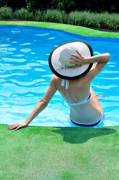 Mujer sexy en sombrero de sol relajante en la piscina, vista trasera . — Foto de Stock