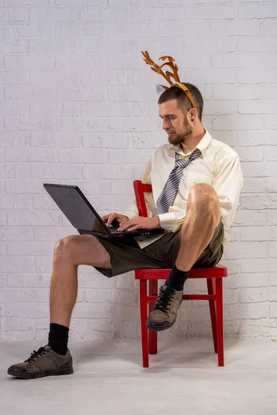Gömlekli Şortlu Neşeli Geyik Boynuzlu Bir Adamı Dizüstü Bilgisayarda Çalışır — Stok fotoğraf