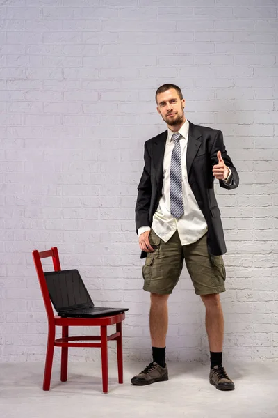 A business man in a business suit and shorts holds a laptop and shows the ok sign. Remote work concept. Freelancer.
