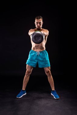 Sportif bir adam siyah arka planda kettlebell ile ağırlık çalışması yapıyor. Yaya geçidi. Kettlebell ile Fitness.