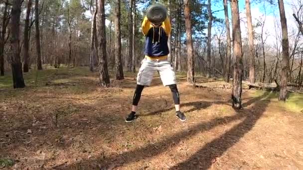 Um jovem treina com uma campainha na floresta. Balança o kettlebell. — Vídeo de Stock