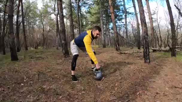 Ein junger Mann trainiert im Wald mit einer Wasserstoffglocke. Werfen mit Wasserkesseln. — Stockvideo