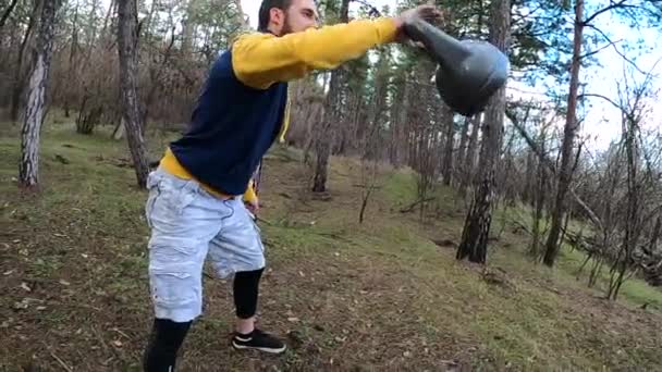 Um jovem treina com uma campainha na floresta. Kettlebell malabarismo. — Vídeo de Stock