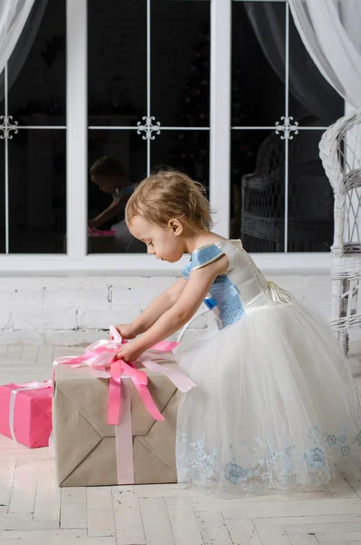 Little girl in a beautiful dress unpacks Christmas gift — Stock Photo, Image