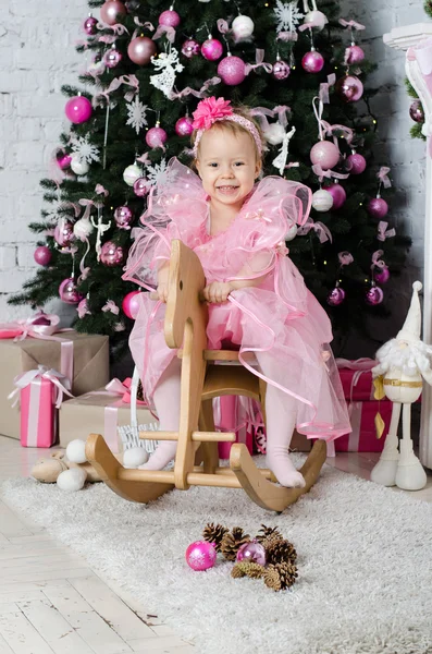 Bella ragazza seduta su un cavallo a dondolo vicino a un albero di Natale — Foto Stock