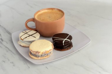 Üç farklı alfajore ile bir fincan kahve. Arjantin tatlı yemekleri. Çikolatalı alfajor. Alfajor de dulce de leche. Beyaz çikolata alfajor.