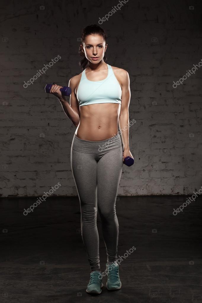 Muscular athletic female in bra, panties and sneakers sitting in balasana  pose, relaxing back after intensive workout with dumbbells in gym.  Unrecognizable woman having rest during training Stock Photo