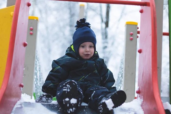 Bir çocuk kışın oyun parkında kayar. Karlı bir kış parkında ceketli bir çocuk oynuyor.. — Stok fotoğraf