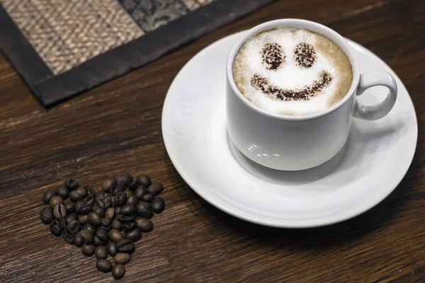 Eine Tasse Kaffee und ein Herz aus Kaffeebohnen auf dem Tisch. — Stockfoto