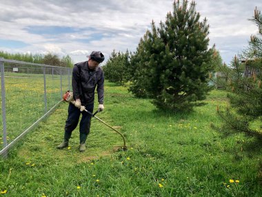 İş kıyafetleri içinde bir erkek bahçıvan çitin yanında gözlerini kısıyor karahindiba yağı buduyor.