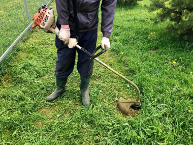 İnşaat alanındaki çimleri biçen bir bahçıvanın elindeki budama benzini. Yakın plan..