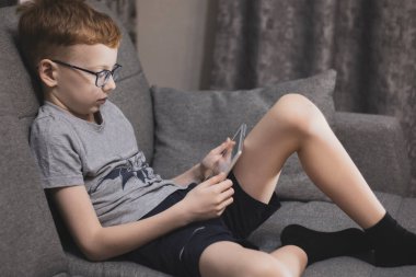 Öngörü için gözlüklü kızıl saçlı bir çocuk tablette oynar, akşamları kanepede oturur..