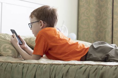 Yatakta yatan genç kız cep telefonuna bakıyor. Taşınabilir İnternet.