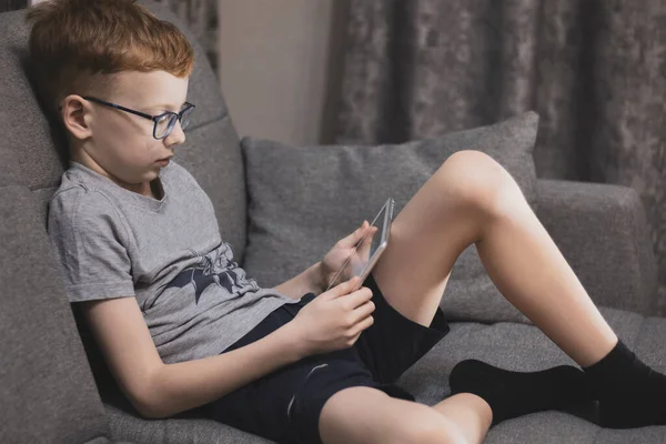 Öngörü için gözlüklü kızıl saçlı bir çocuk tablette oynar, akşamları kanepede oturur..