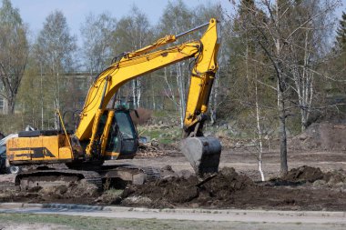 Toprağı yerinden oynatan kova ile donatılmış bir makine zemini geliştiriyor, yol yapımı var. İnşaatın devamı için site hizalanıyor.