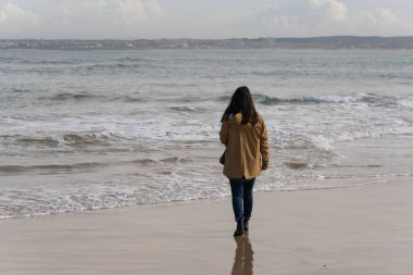 Portekiz, Peniche 'de sarı ceketli bir kadın sahilde yürüyor.