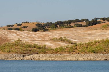 Portekiz, Terena 'da mavi gökyüzü olan baraj gölü rezervuarındaki suya yansıyan tepe manzarası gibi çöl.