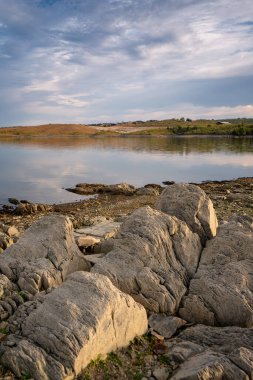 Terena 'daki Lucefecit Barajı göl rezervuarı ve ön planda Portekiz' deki kayaları yansıtıyor.