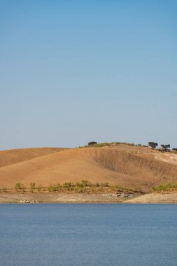 Portekiz, Terena 'da mavi gökyüzü olan baraj gölü rezervuarındaki suya yansıyan tepe manzarası gibi çöl.