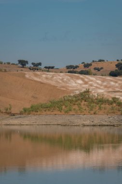 Portekiz, Terena 'da mavi gökyüzü olan baraj gölü rezervuarındaki suya yansıyan tepe manzarası gibi çöl.