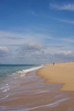 Portekiz 'de kumsalda okyanus dalgaları olan Comporta' da balık tutan bir balıkçı.