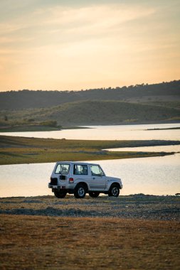 4x4 araba gün batımında Alentejo, Portekiz 'deki güzel kahverengi manzaralı bir gölde.