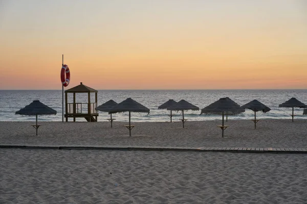 Portekiz, Comporta 'da gün batımında boş bir plaj ve saman yaz şemsiyeleri.